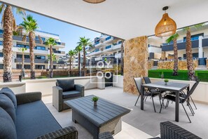 Une terrasse extérieure moderne, avec des meubles en osier, un pilier en pierre et une vue sur un quartier résidentiel agrémenté de palmiers et de bâtiments.