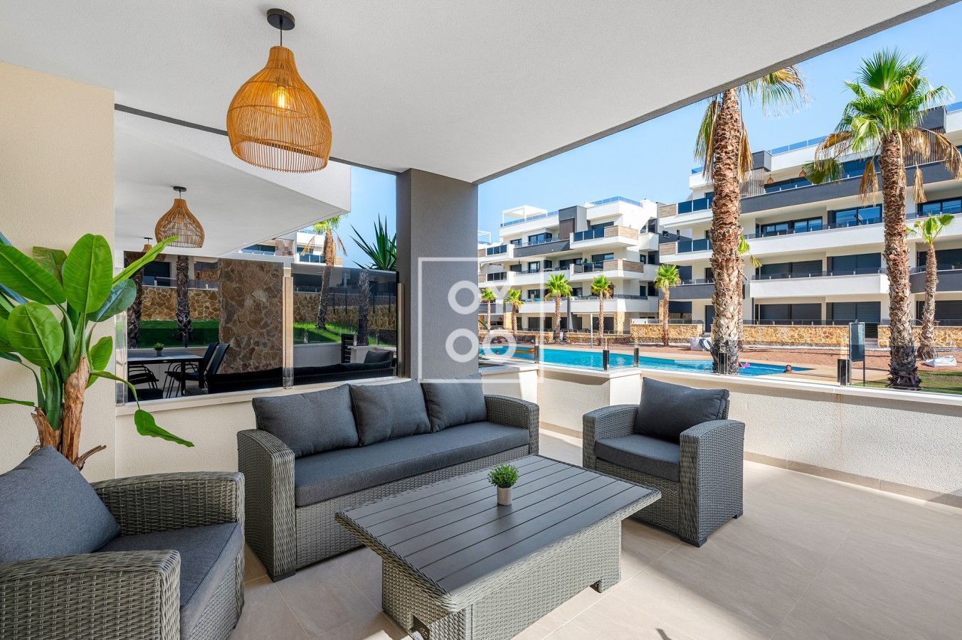 A modern outdoor seating area with wicker furniture, a pool, and a view of a multi-story building with balconies.