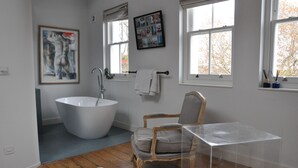 A modern bathroom with a freestanding bathtub, a wooden chair, and a clear glass table. - Design-Led Islington Home with Huge Private Garden (London)