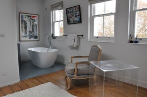 Een moderne badkamer met een vrijstaand bad, een houten stoel en een glazen bijzettafeltje.