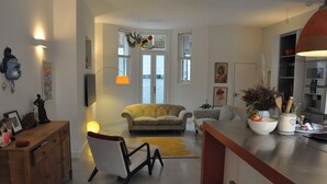 A spacious living area with a sofa, a dining table, and a kitchen area with cabinets and a stove. - Design-Led Islington Home with Huge Private Garden (London)