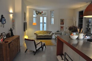 Een ruime woonkamer met een bank, een eettafel en een keuken voorzien van kastjes en een fornuis.
