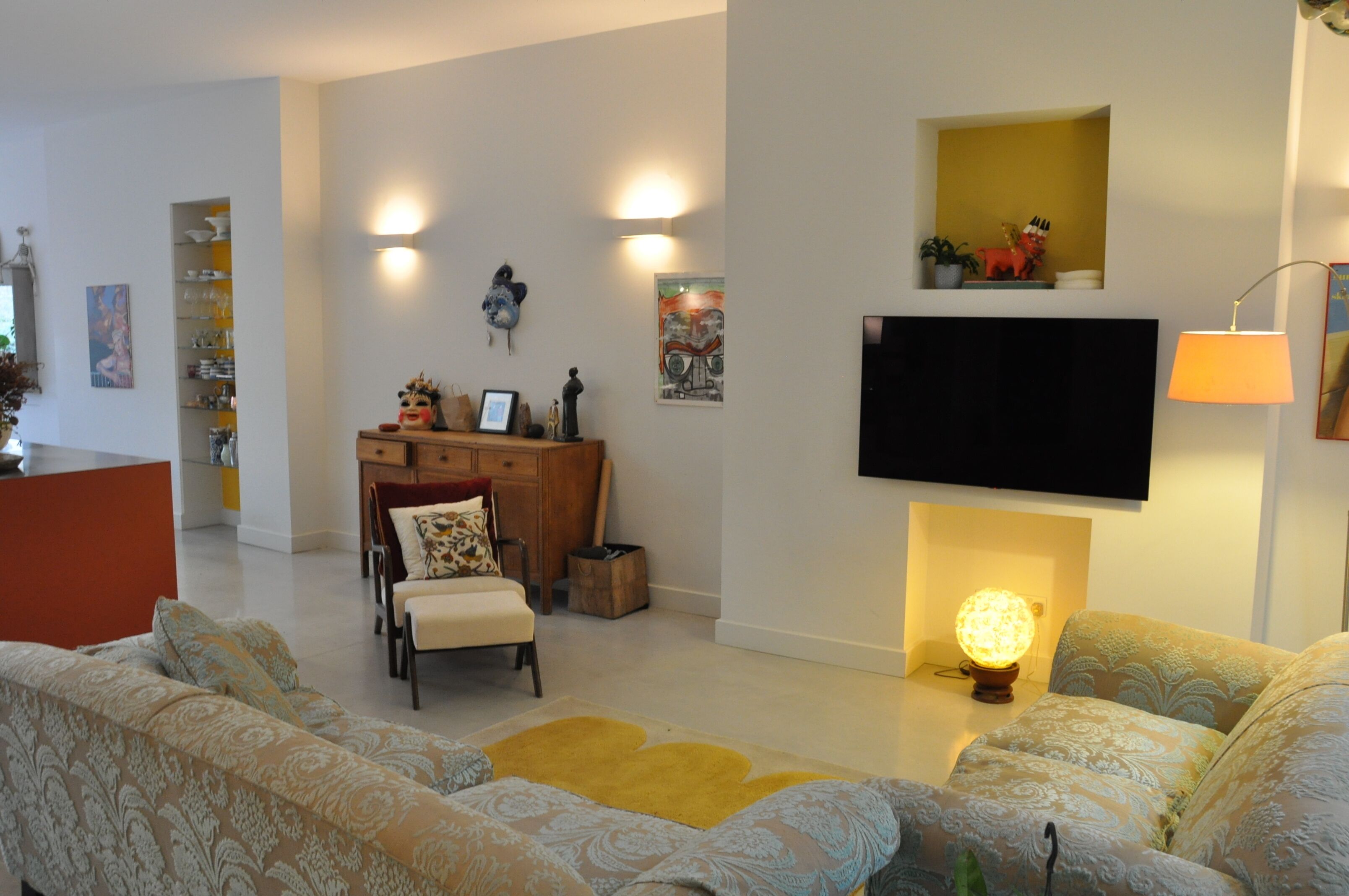A modern living room with a sofa set, a flat-screen TV mounted on the wall, and a fireplace with a decorative light.