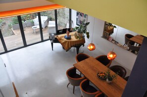 A dining area with a wooden table, chairs, and a view of the outdoors through large windows. - Design-Led Islington Home with Huge Private Garden (London)
