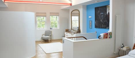 Une chambre à coucher moderne avec un grand lit, un bureau, une chaise, une fenêtre et un tableau au mur.