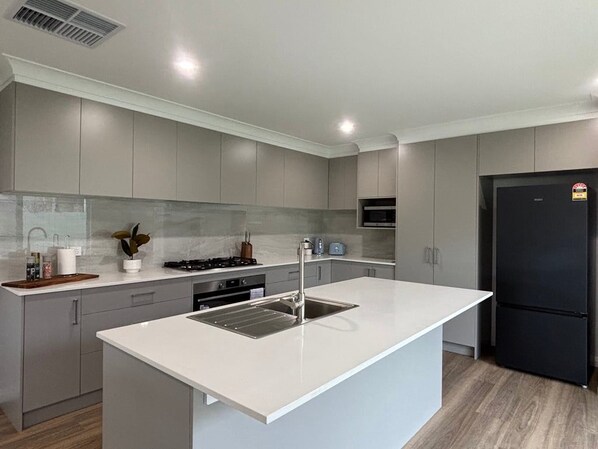 A modern kitchen with grey cabinetry, a white countertop, stainless steel sink, and a black refrigerator.