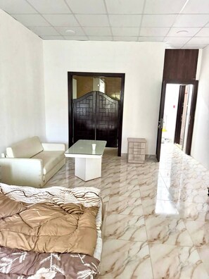 A hotel room with a bed, a sofa, a small table, and a bathroom visible through a door. - Studio Flat Near Al-khalidi Hospital French Embassy (Amman)