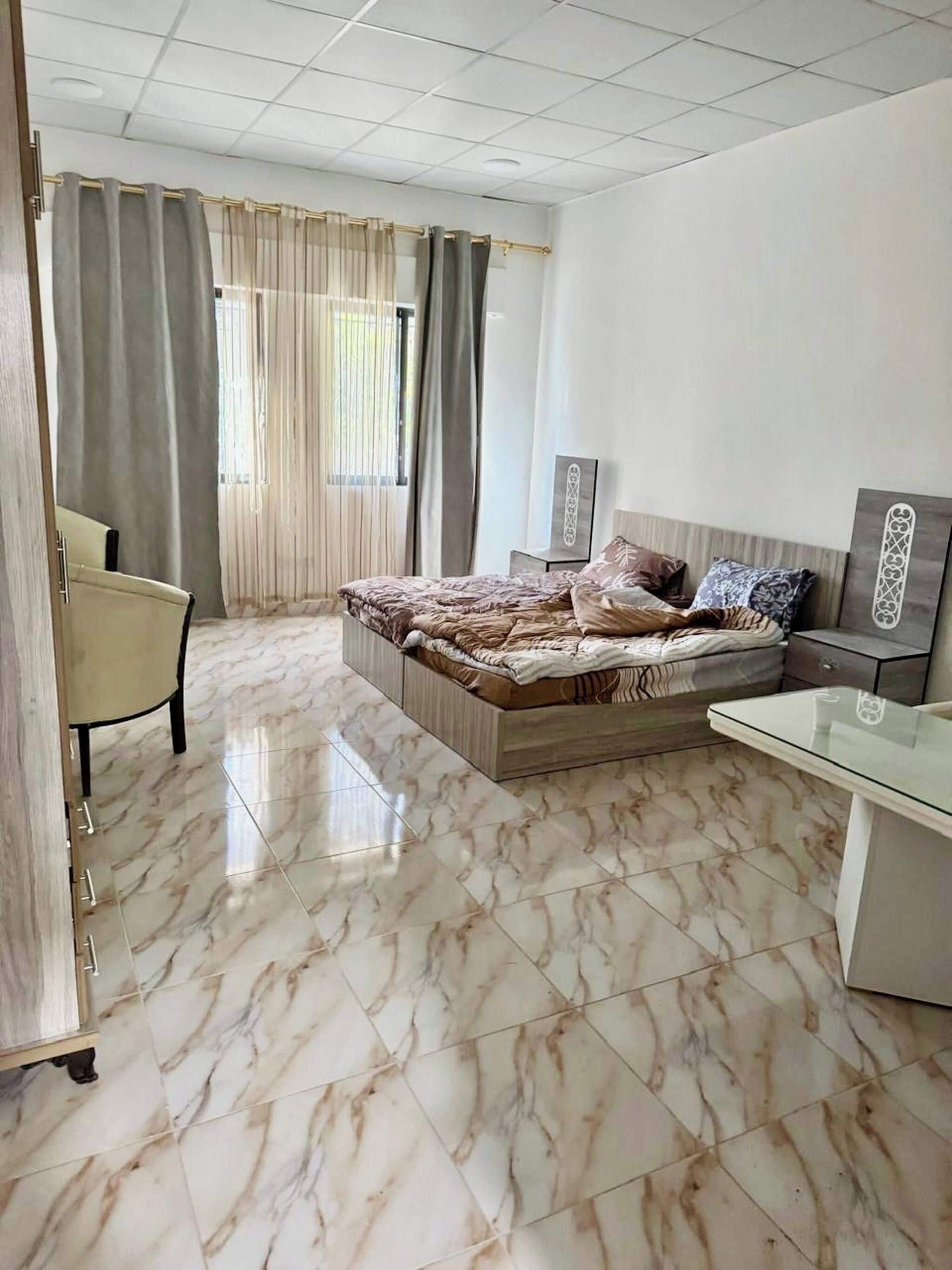 A hotel room with a bed, a desk, a chair, and a window with curtains.