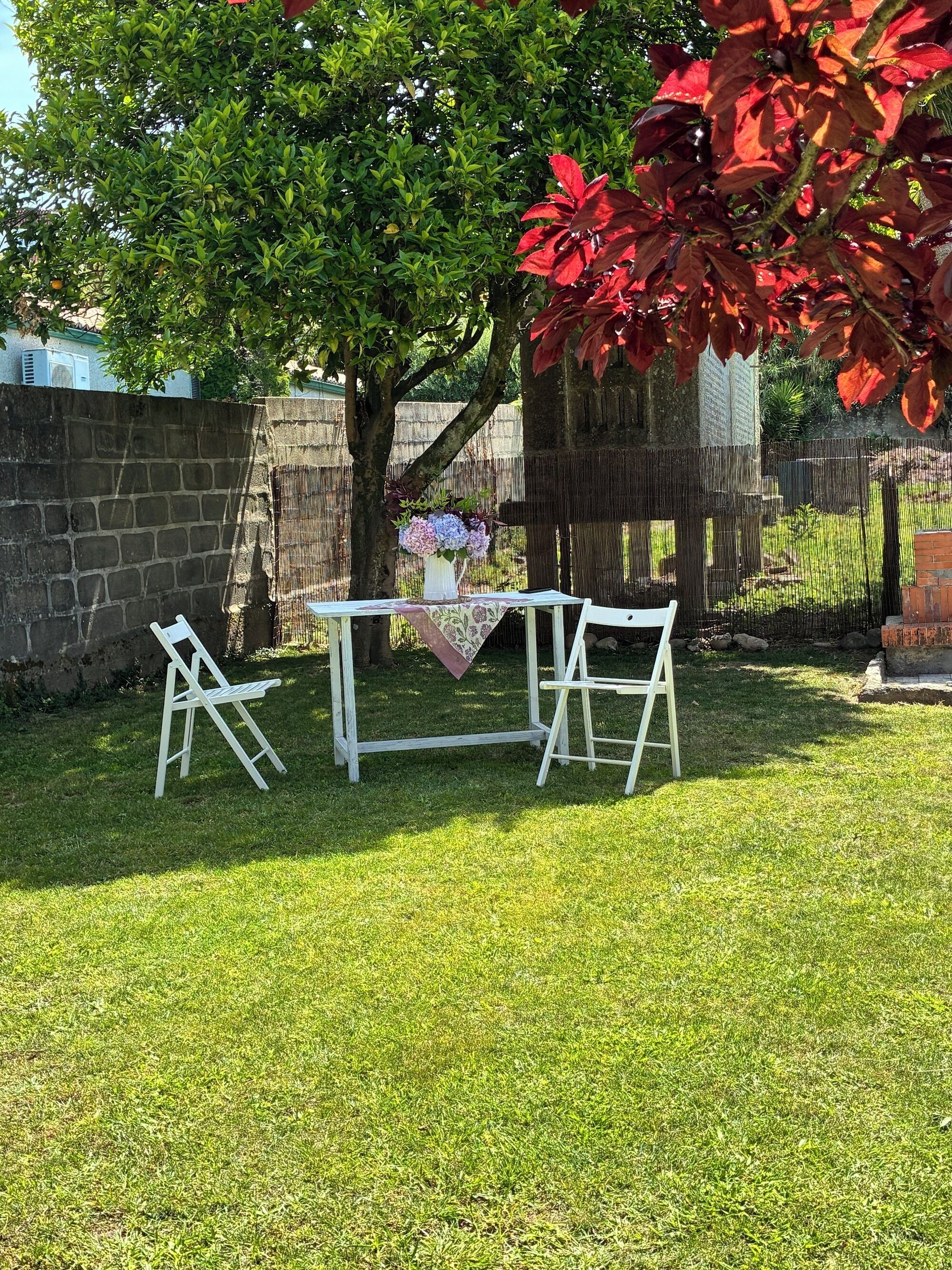 Un área de estar al aire libre con una mesa y sillas, rodeada de césped y una cerca de madera.