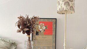 Ein Nachttisch aus Holz mit einem gerahmten Bild, einer Vase mit getrockneten Blumen und einer Lampe.