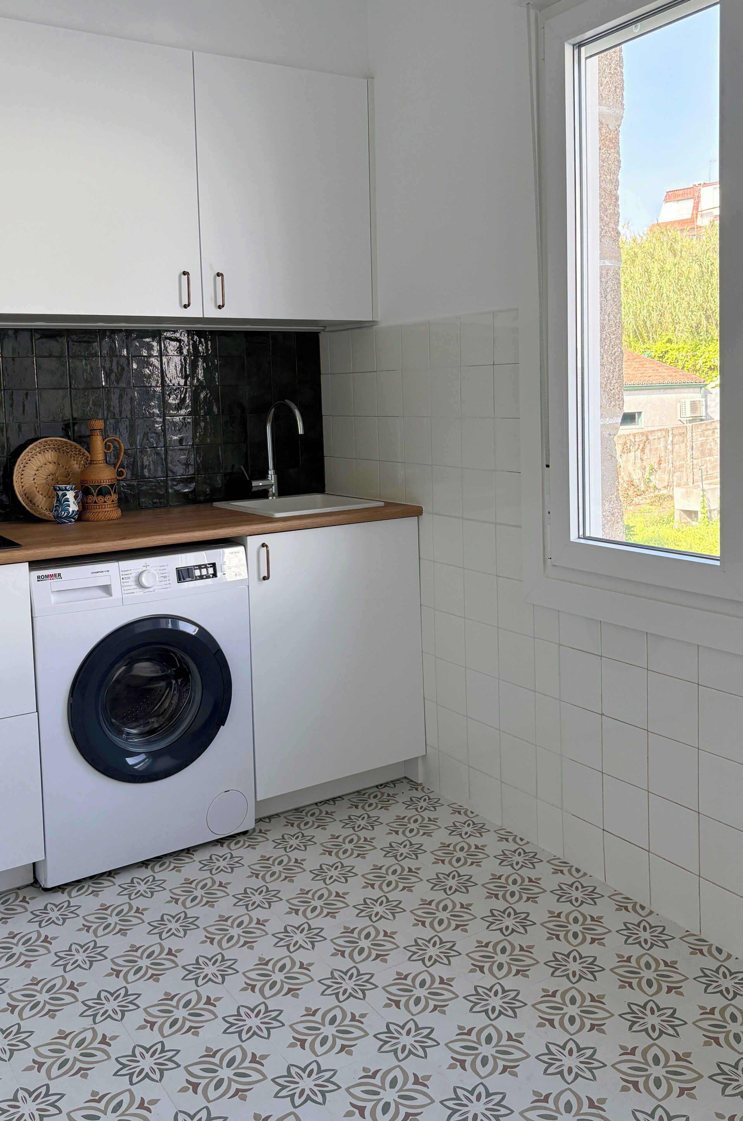 Cocina compacta con lavadora, lavaplatos y ventana con vista a edificios.