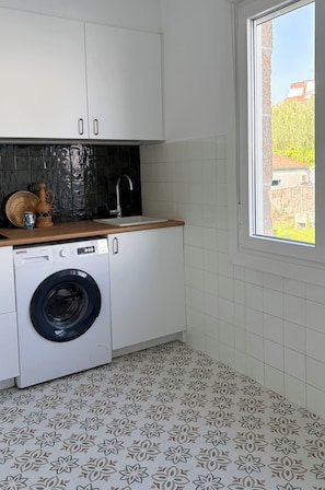 Cocina compacta con lavadora, lavaplatos y ventana con vista a edificios.