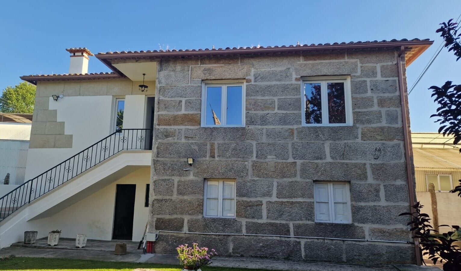 Ein zweistöckiges Steinhaus mit Treppe, Balkon und kleinem Garten.