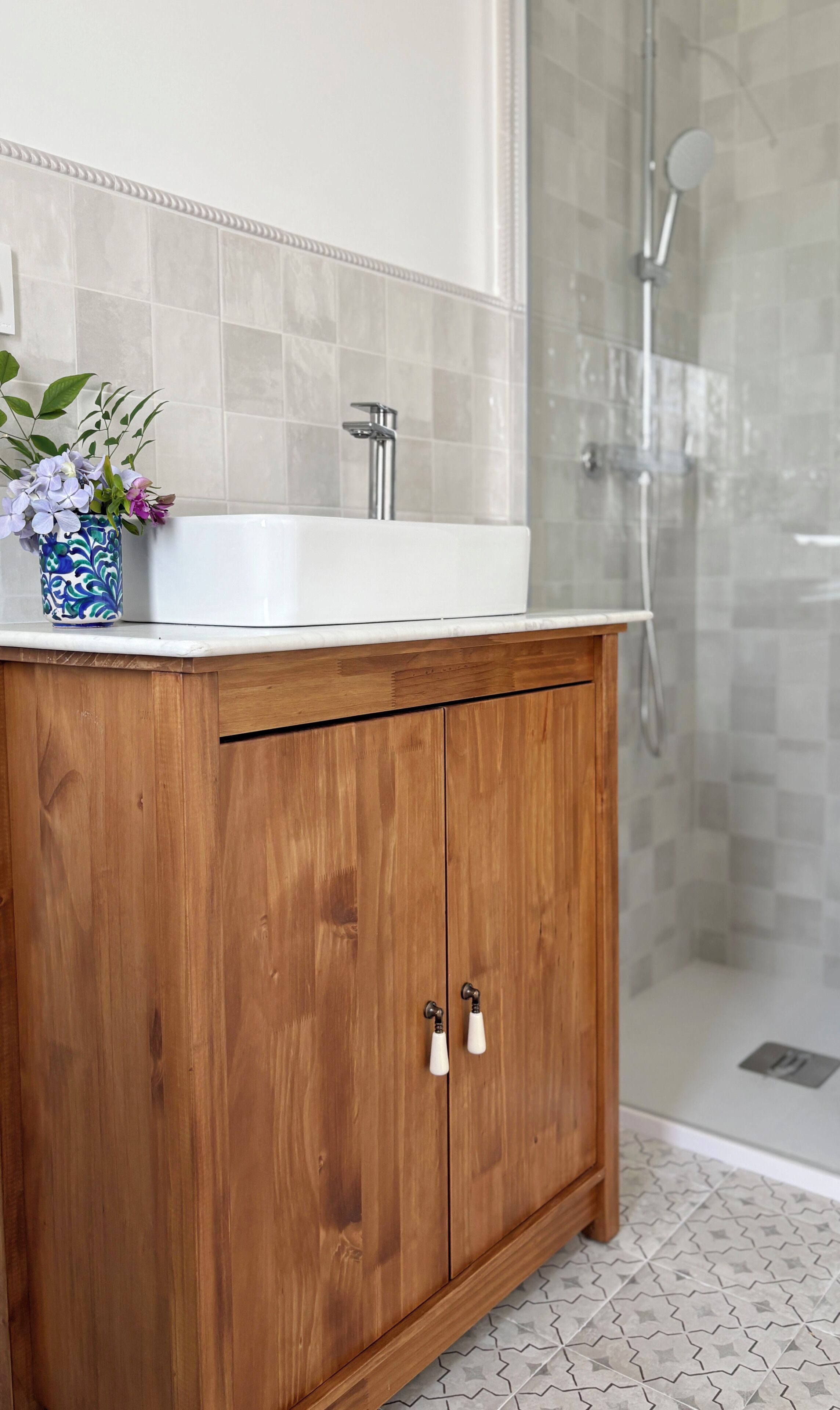 Ein Badezimmer mit einem Holzbadezimmermöbel, einem weißen Waschbecken und einem Duschbereich.