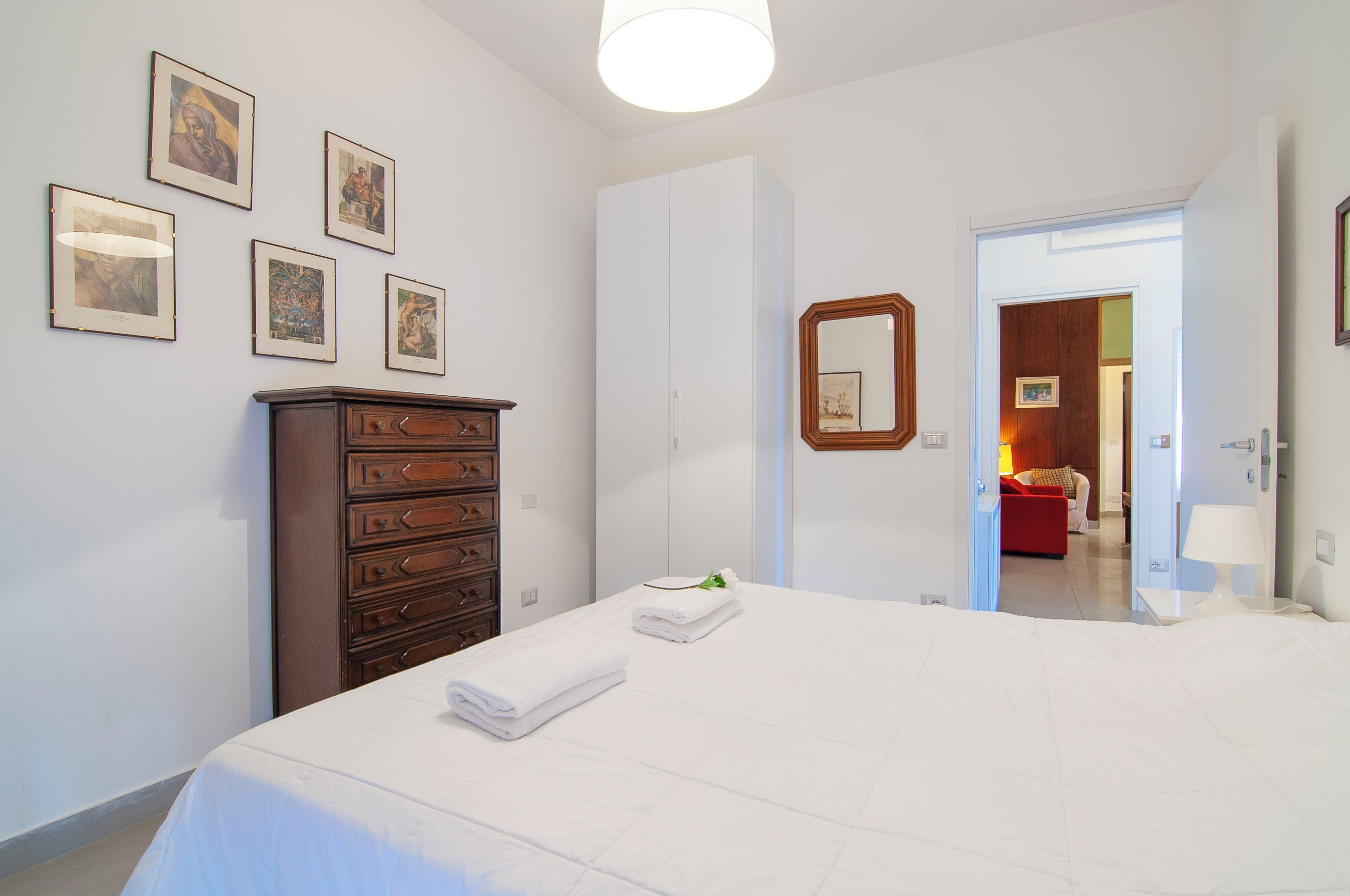 A hotel room with a bed, a dresser, and framed pictures on the wall.