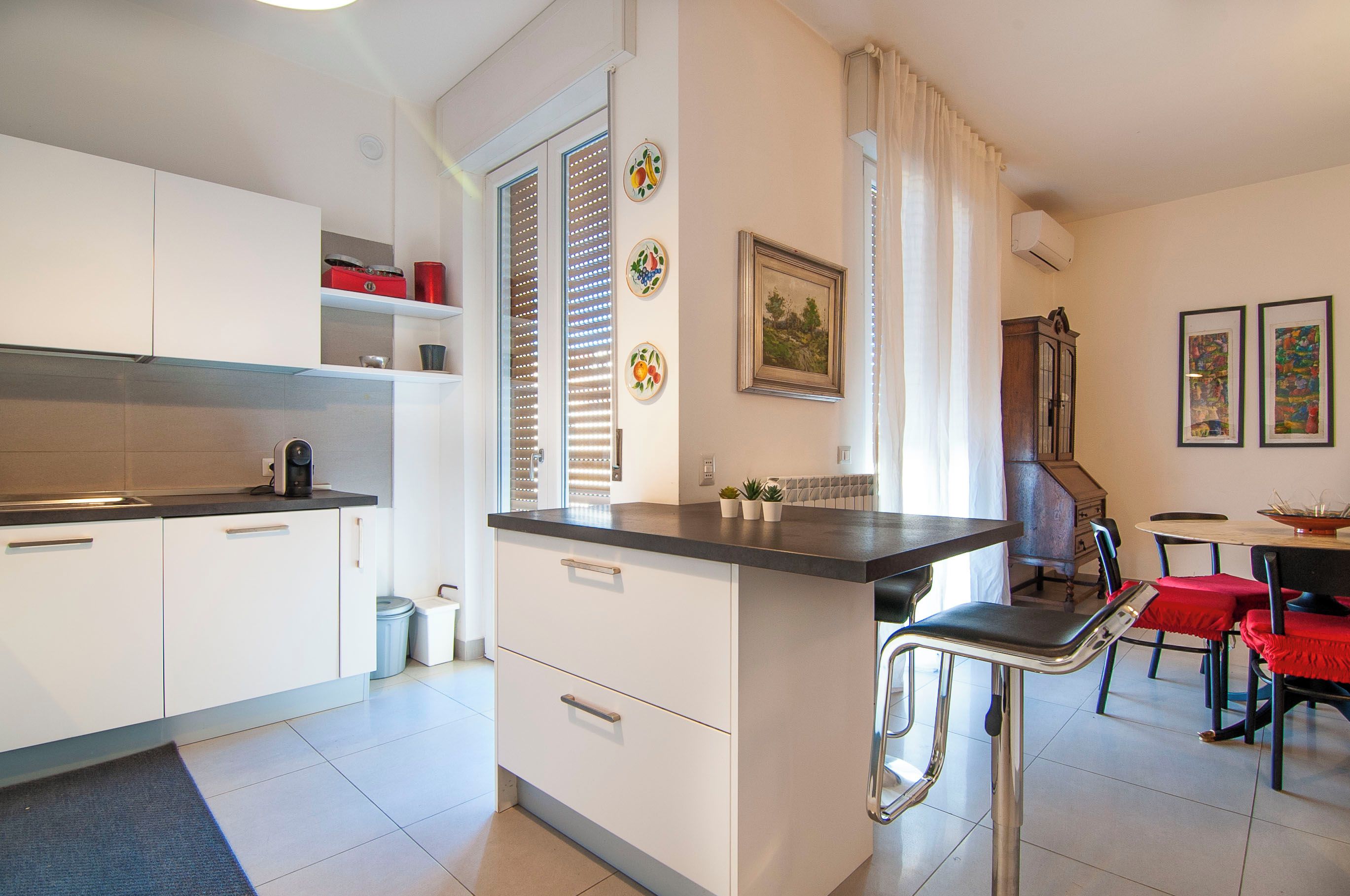 A modern kitchen with white cabinetry, a coffee machine, and a dining area with a table and chairs.
