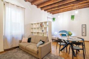 A furnished room with a sofa, a dining table with chairs, a bookshelf, and a bed with a headboard. - Kedimore - RomeoHouse (Verona)