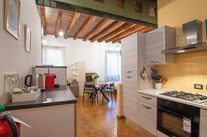 A compact kitchen with a gas stove, a coffee machine, and a dining area with a table and chairs. - Kedimore - RomeoHouse (Verona)