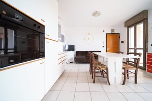 Une cuisine moderne avec des meubles blancs, un four encastré et un coin repas comprenant une table blanche et des chaises en bois.