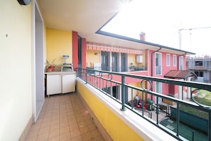 Ein Balkon mit Fliesenboden, ein kleiner Küchenbereich mit Schränken und Blick auf benachbarte Gebäude.