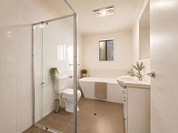Een moderne badkamer met een douchecabine van glas, een toilet, een bad en een wastafel.
