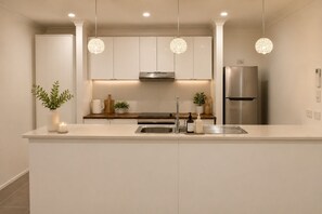 Een moderne keuken met een centraal eiland, roestvrijstalen apparatuur, hangende lampen en een strak, minimalistisch design.
