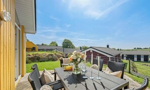 Eine Terrasse im Freien mit Esstisch, umgeben von Korbstühlen und einer Zierdecke mit Blumen.