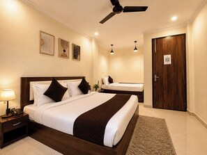 A hotel room with a large bed, bedside tables, a ceiling fan, and a door with a QR code. - Rukamni INN (Vrindavan)