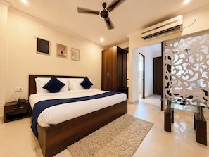 Un dormitorio moderno con cama, mesitas de noche, ventilador de techo, aire acondicionado y un separador decorativo.