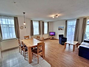 Ein modernes Wohnzimmer mit einem Holzesstisch, Stühlen, einem Fernseher und einem Sofa.
