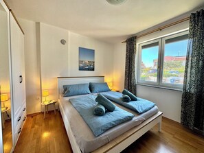 A bedroom with a bed, bedside tables, a window with curtains, and a painting on the wall. - "FeWo Silke" Vacation Rental with Air Conditioning, Wi-Fi, and Parking (Krk)