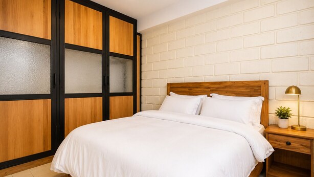 A bedroom with a bed, nightstand, and a wardrobe with frosted glass panels. - Mwalosun Luxury Vintage Apartment101 (Kampala)