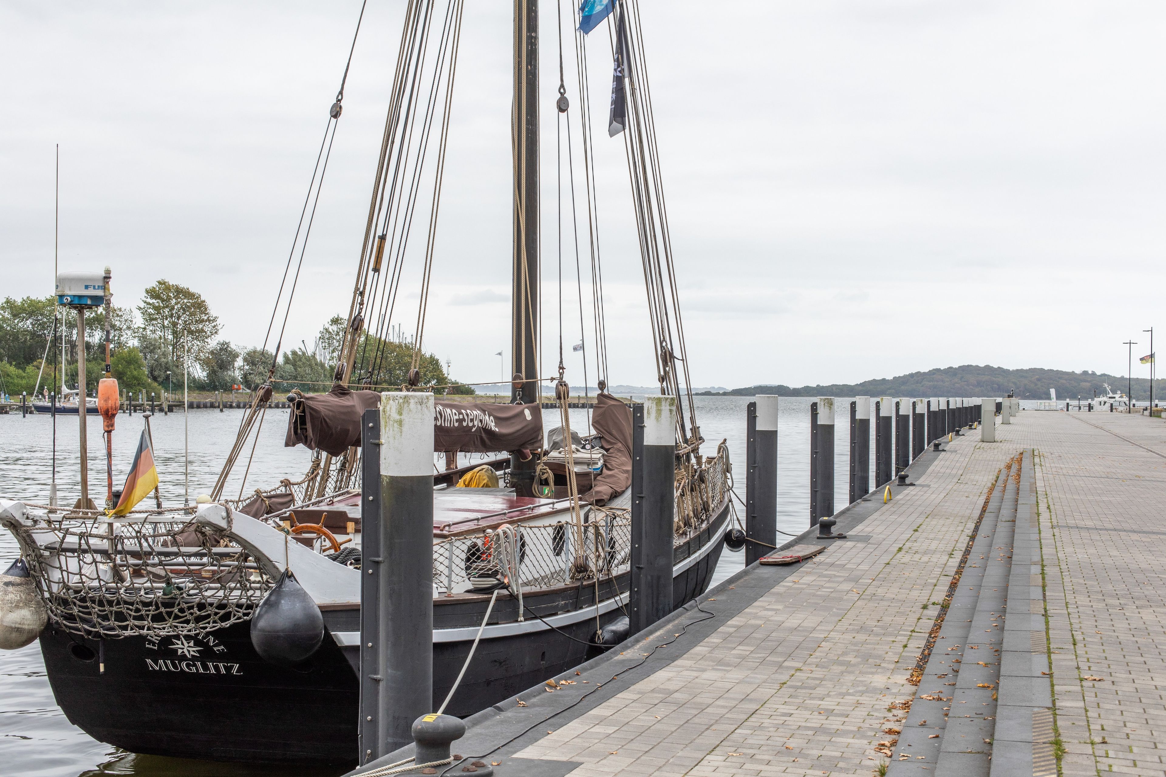 En förtöjd segelbåt med namnet ”MUGLITZ”, utrustad med ett nät i fören, rep och en flagga.