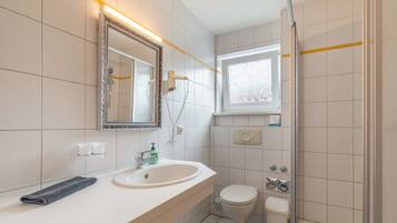 Een badkamer met een wit wastafel, een spiegel, een toilet en een douchehoek.