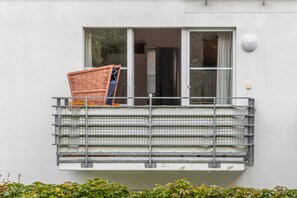 A balcony with a metal grill, a wicker chair, and a window with curtains.