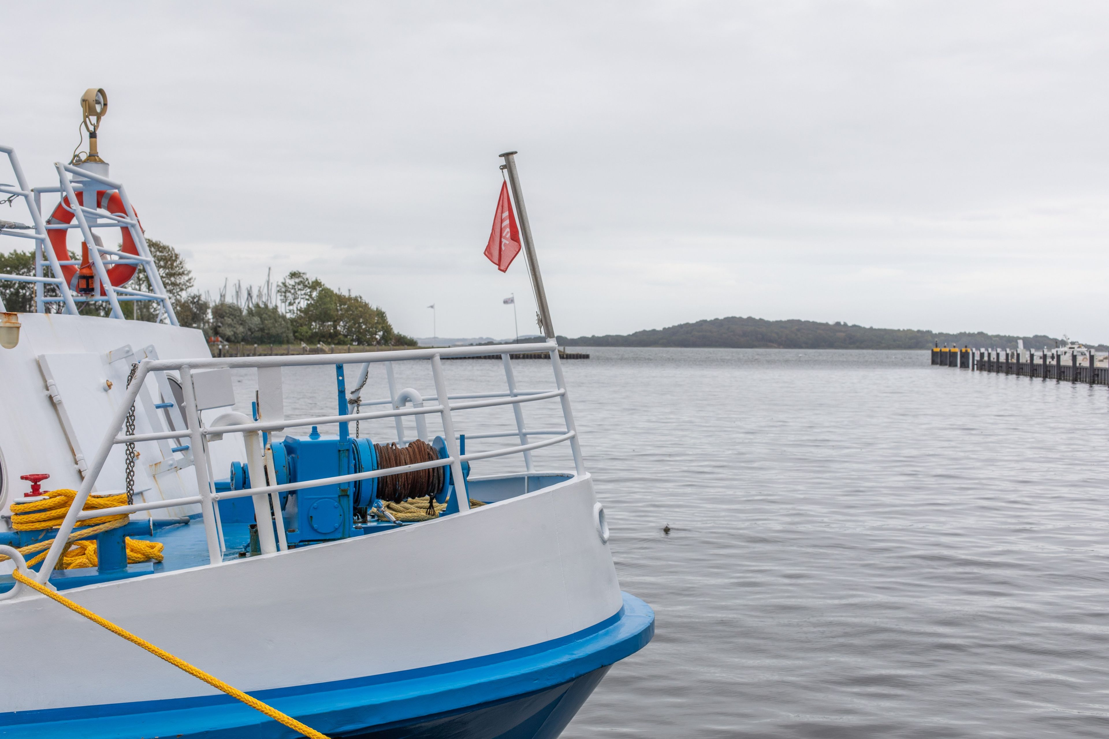 Ein Boot liegt an einem Steg, mit einem Rettungsring und einer roten Flagge auf dem Deck.