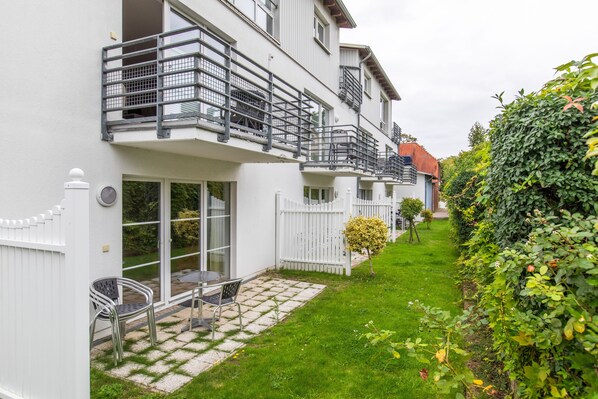 A residential building with a balcony, a small patio with outdoor furniture, and a well-maintained garden.