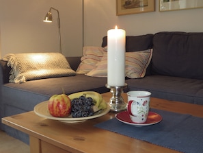 Sala de estar aconchegante com um sofá, uma mesa com uma travessa de frutas, uma vela e uma xícara.