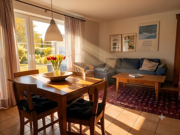 Sala de estar com mesa de jantar, cadeiras, sofá, mesa de centro e vista para o exterior através de grandes janelas.