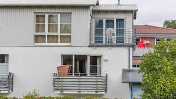 A two-story building with a balcony, a window with a metal grill, and a door.