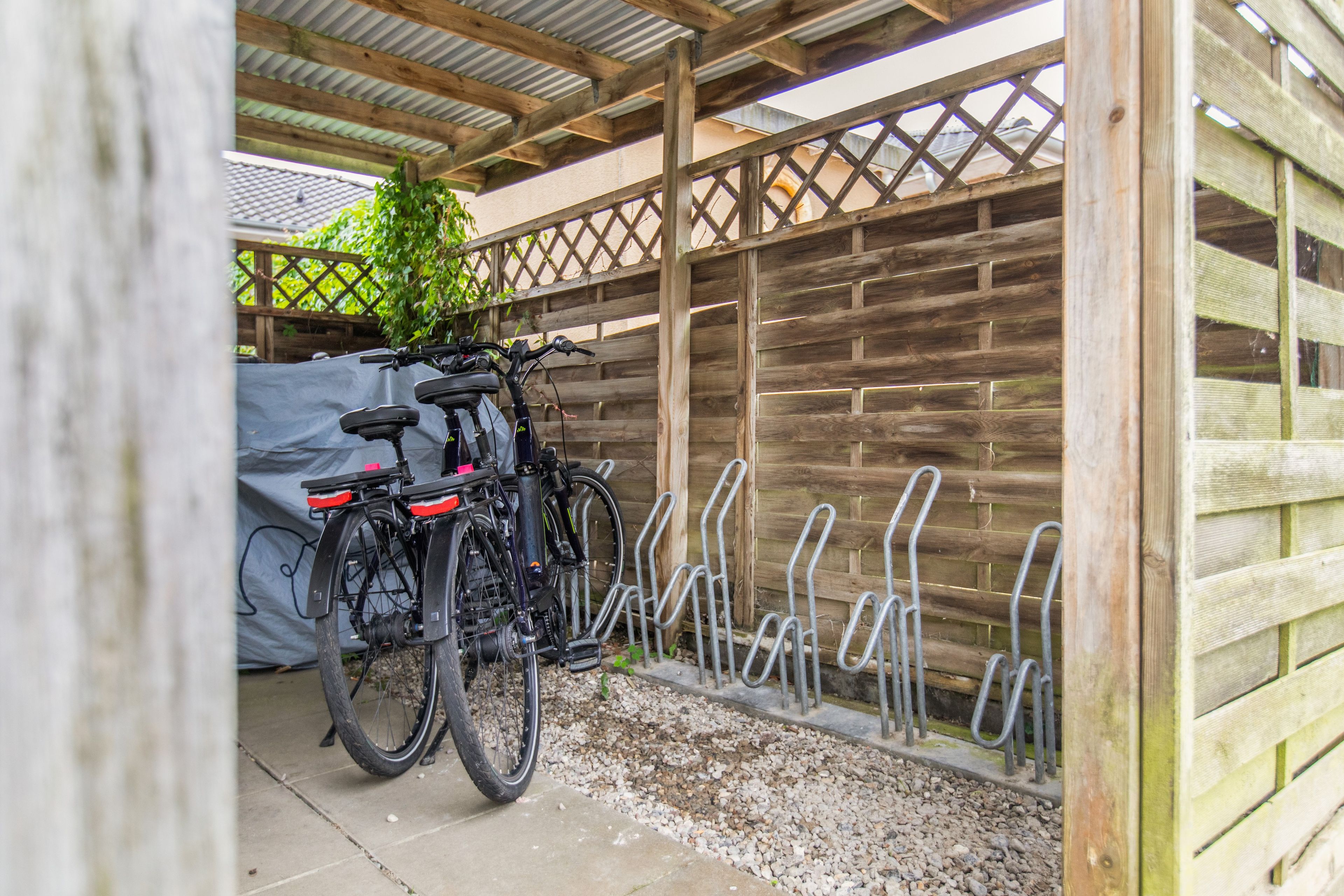 Ein überdachter Außenbereich mit Holzlattenzaun, Fahrradständer und überdachtem Fahrrad.
