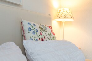 A bed with a white pillow featuring embroidered flowers and a white bedspread.