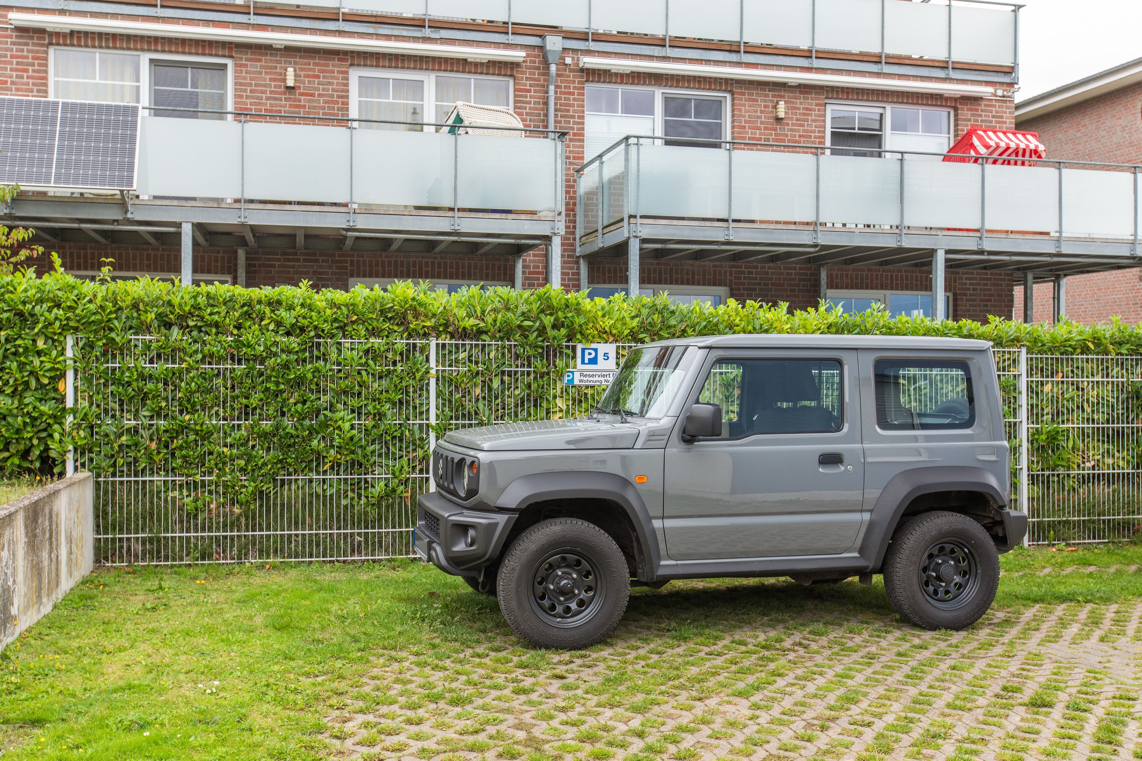En grå SUV står parkerad på en uppfart med en byggnad i tegel som syns i bakgrunden.