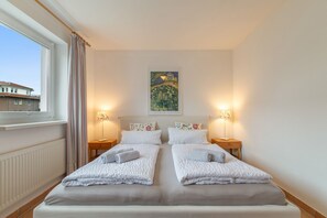 A double bed with two pillows, a bedside table with a lamp, and a painting on the wall.