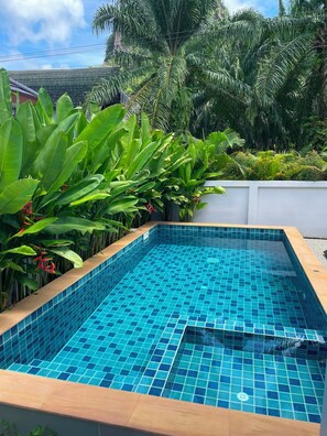 A rectangular swimming pool with blue tiles, surrounded by lush greenery and a white wall. - Natural Pool Villa Ao nang (Mueang Krabi)