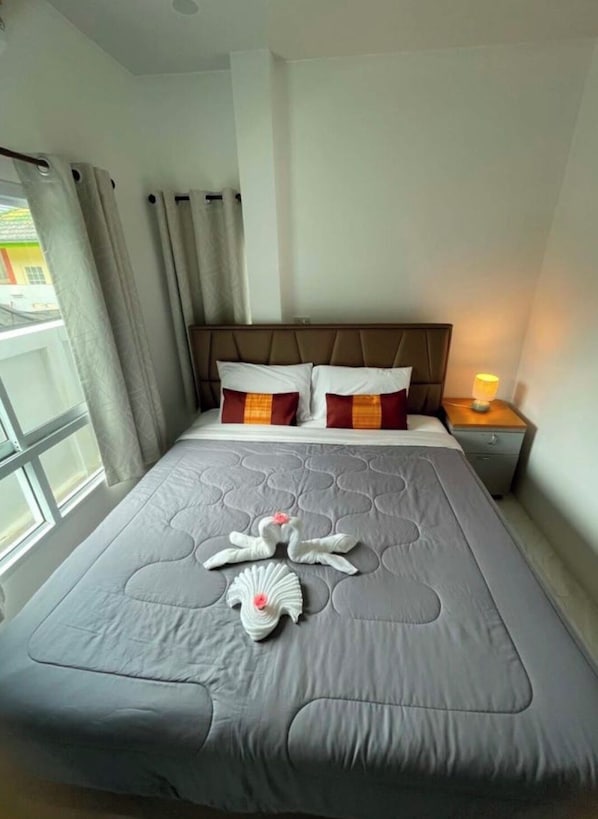 A hotel room with a bed, curtains, a nightstand with a lamp, and a window with a view.