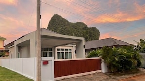 Ein modernes Haus mit einer überdachten Veranda, einem weißen Zaun und einem roten Tor.