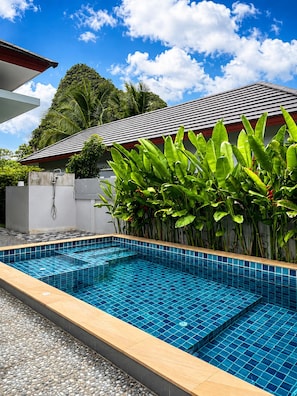 A swimming pool with blue tiles, surrounded by a concrete deck and a white wall.