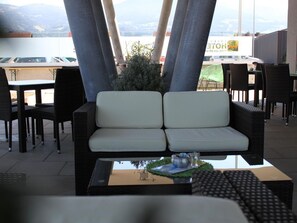 Ein Sitzbereich mit einer Couch und Stühlen, ein kleiner Tisch mit einer Tastatur sowie ein Blick auf den Parkplatz und die Berge im Hintergrund.