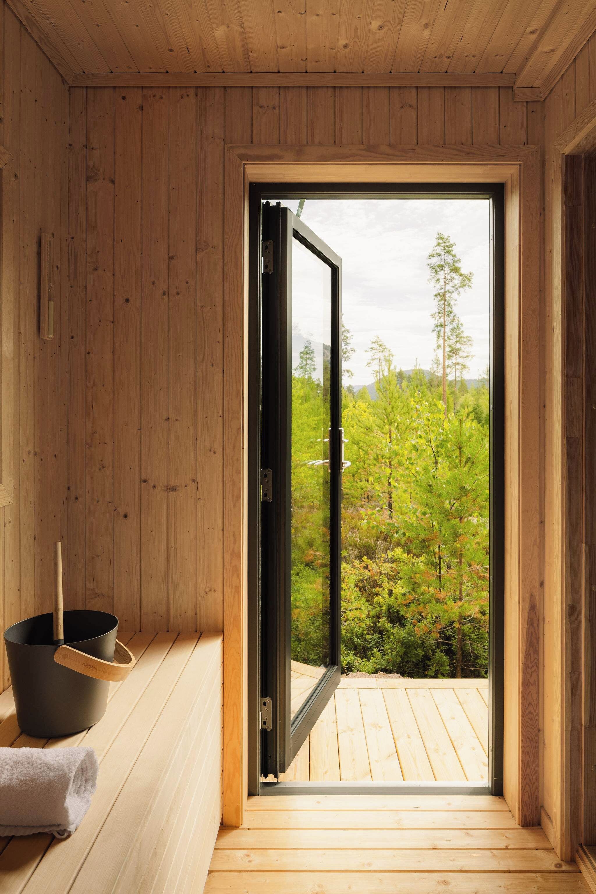 Un sauna de madera con una amplia puerta corrediza que da a un área exterior con vegetación.
